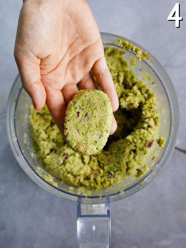 hand holding a green broccoli nugget over food processor