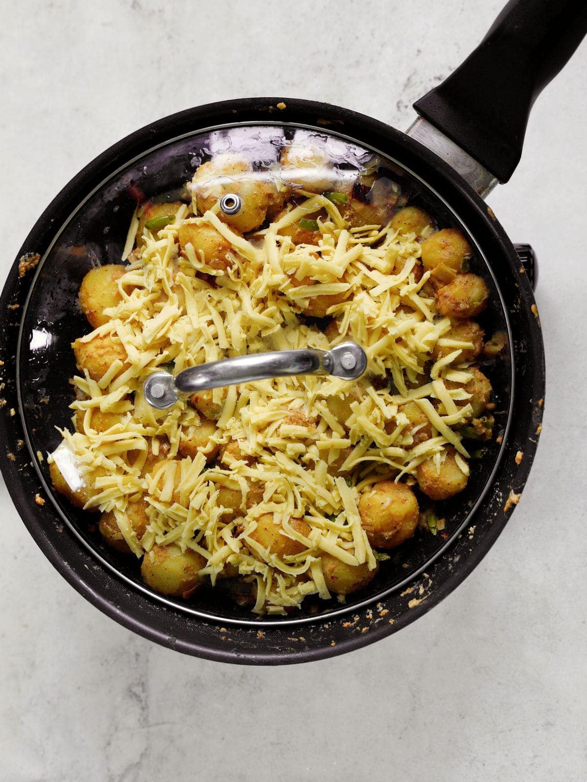 mini boiled potatoes in black skillet topped with cheese and covered with lid