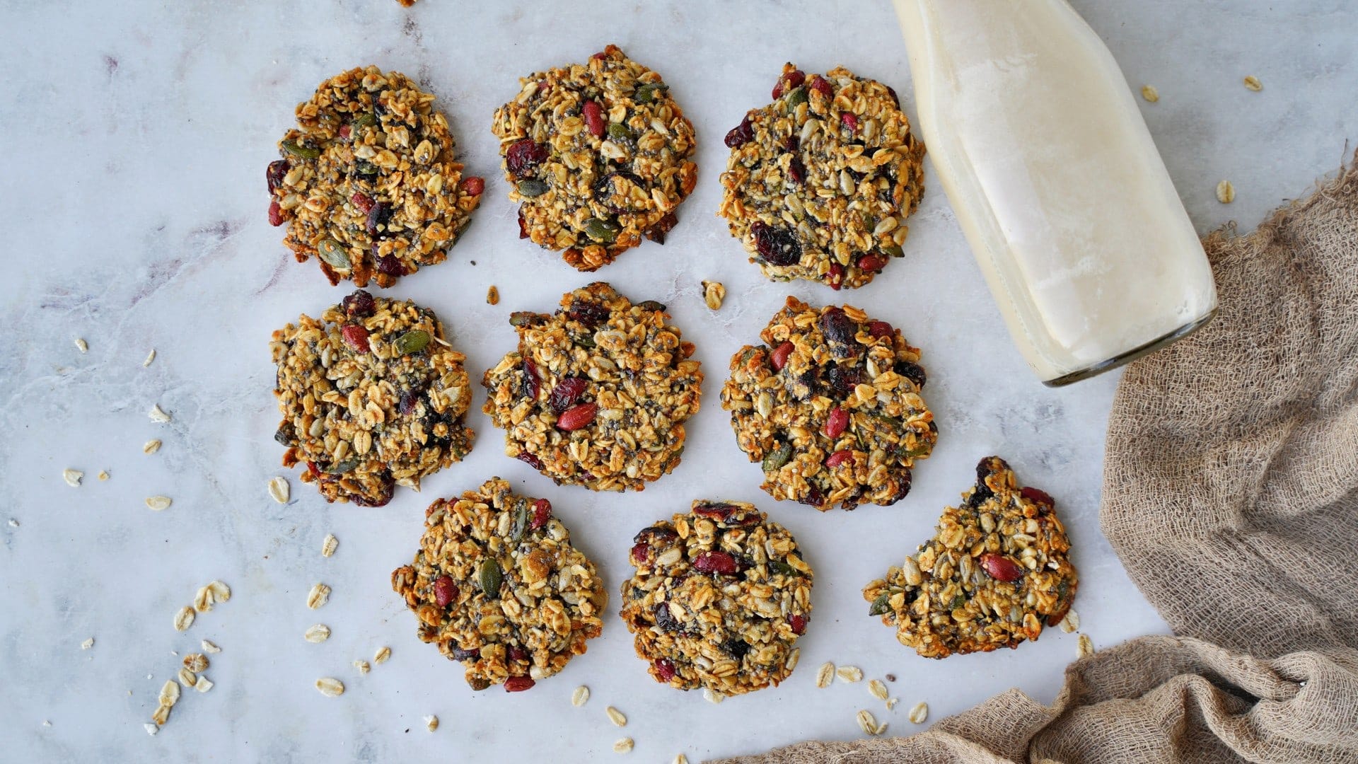 horizontal shot of 9 healthy cookies with oats, seeds, and dried fruit on marble background