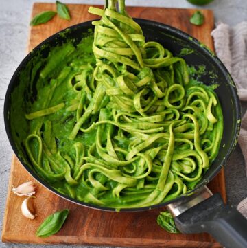 spinach pasta in black skillet with tongs