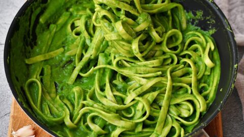 spinach pasta in black skillet with tongs
