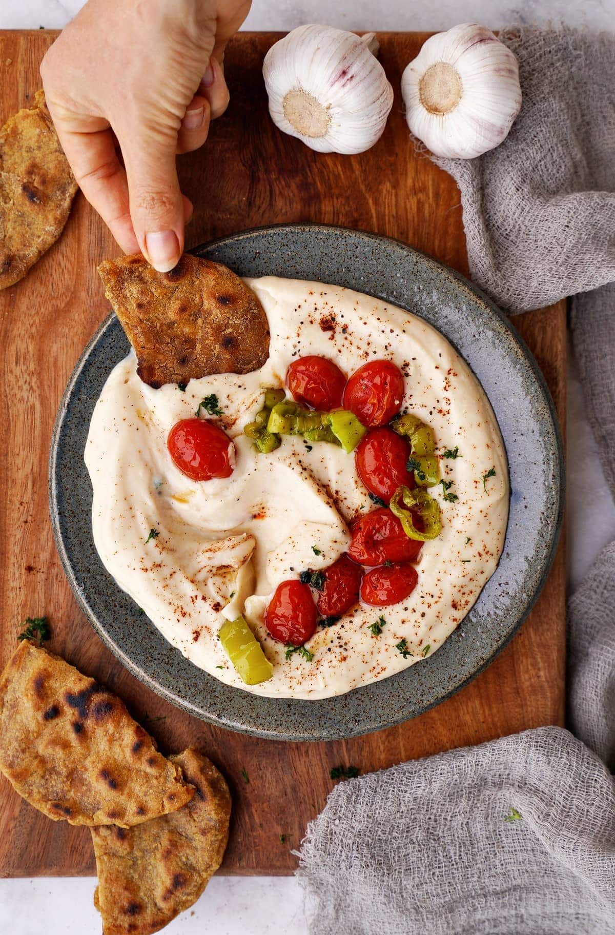 white bean dip with roasted garlic, tomatoes and pepper in bowl with flatbread in hand