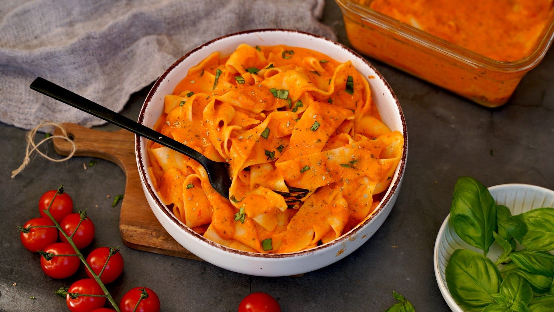 horizontal shot of veggie cream cheese pasta in bowl with basil and tomatoes