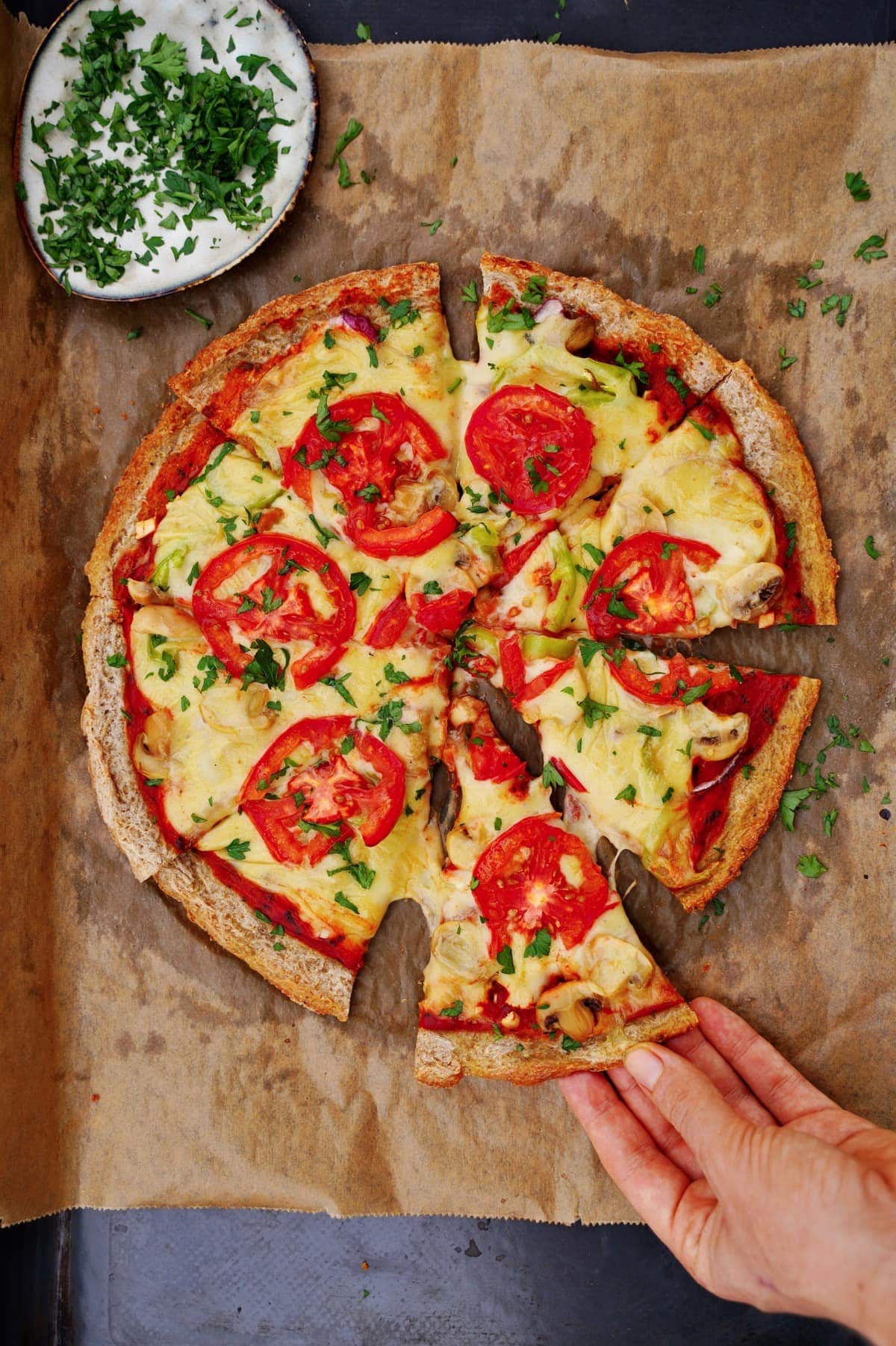 Hand greift nach einem Stück veganer Pizza mit Käse und Gemüse