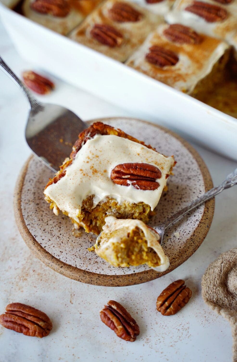 ein Stück Baked Oatmeal mit Kürbis auf einem kleinen Teller mit Löffel und Pekannüssen