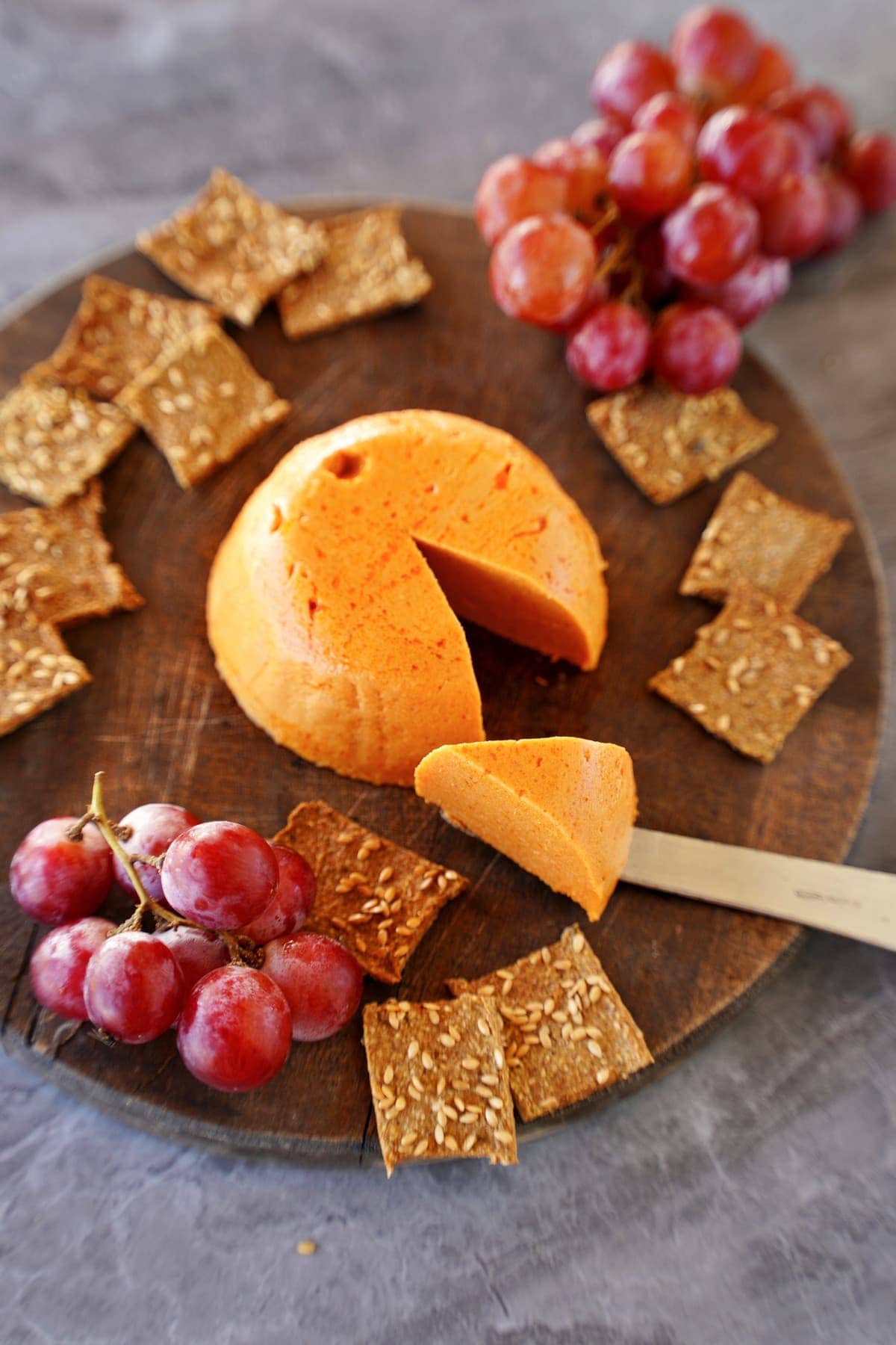 Vegan cheddar cheese with slice cut out with crackers and grapes