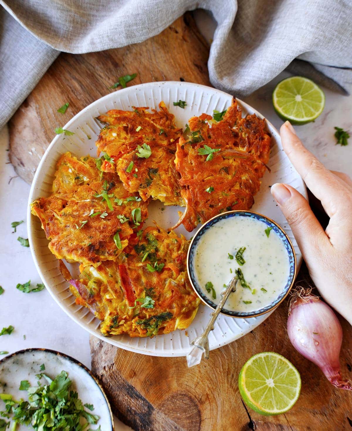 4 Indian veggie fritters on white plate with raita dip