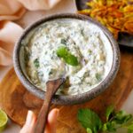 cucumber raita in bowl with wooden spoon