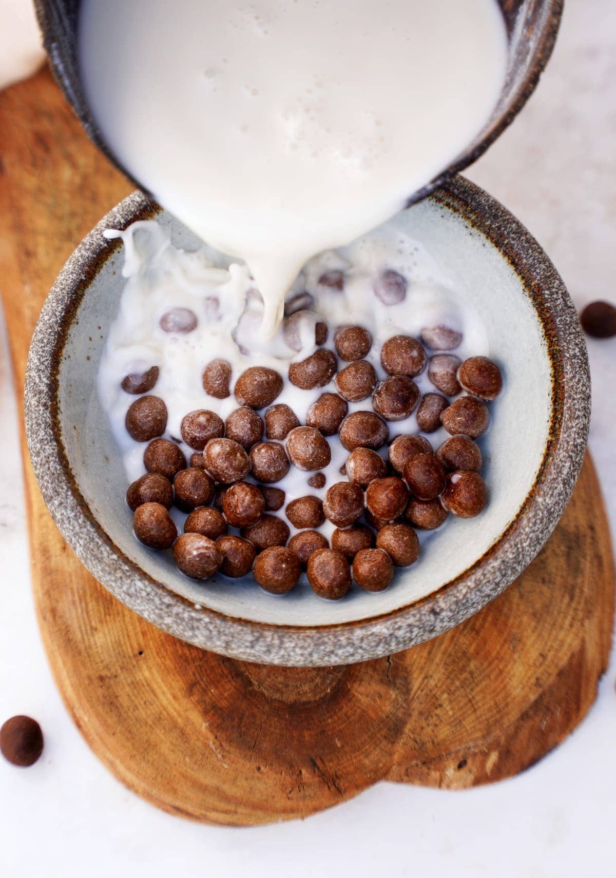 pouring dairy-free milk into bowl with homemade chocolate cereal (cocoa puffs)
