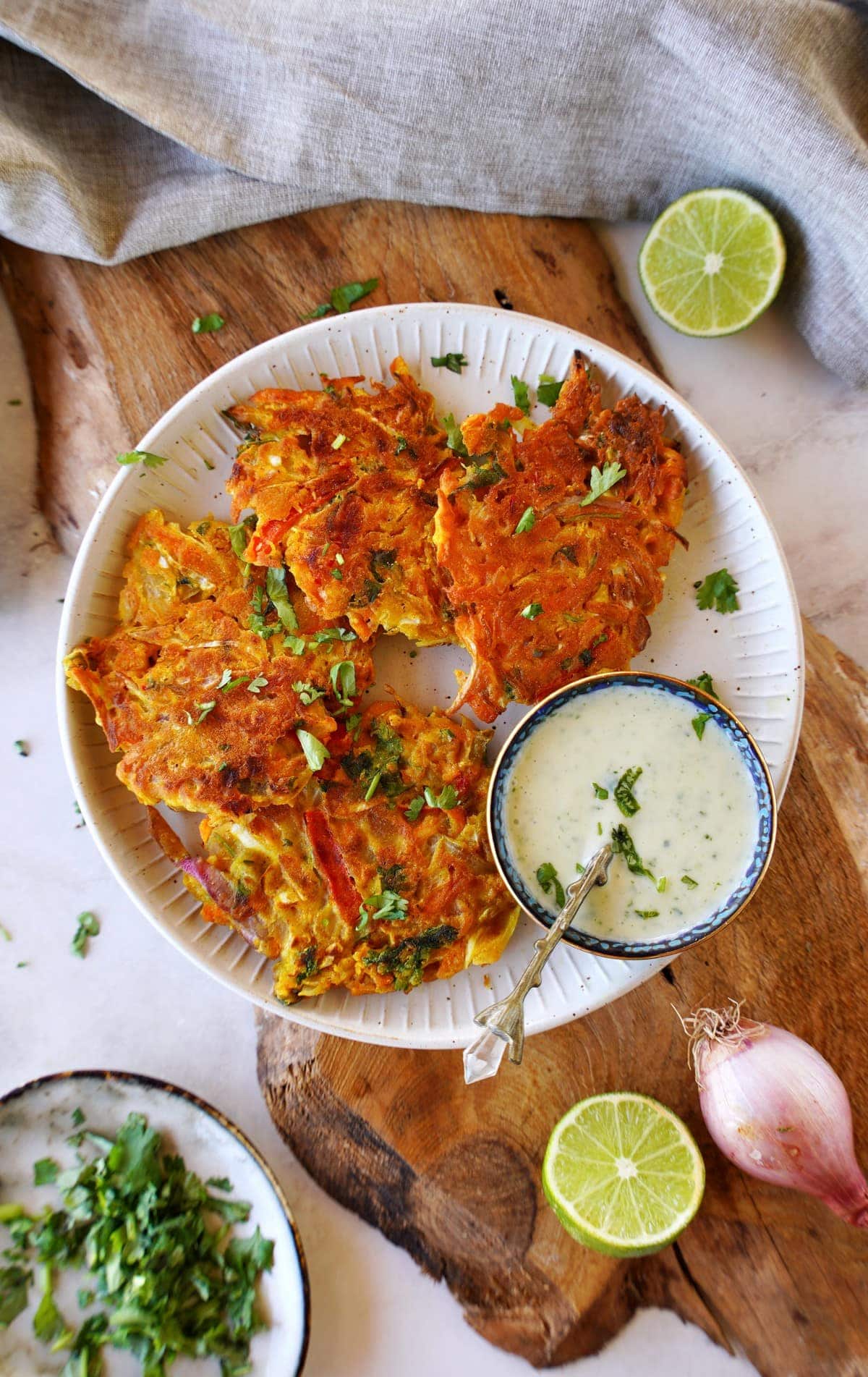 top shot of 4 Indian veggie fritters on white plate with raita dip