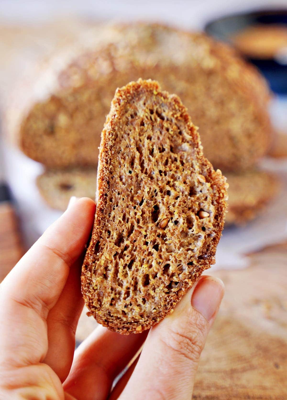 Hand hält eine kleine Scheibe selbstgebackenes kohlenhydratarmes Brot