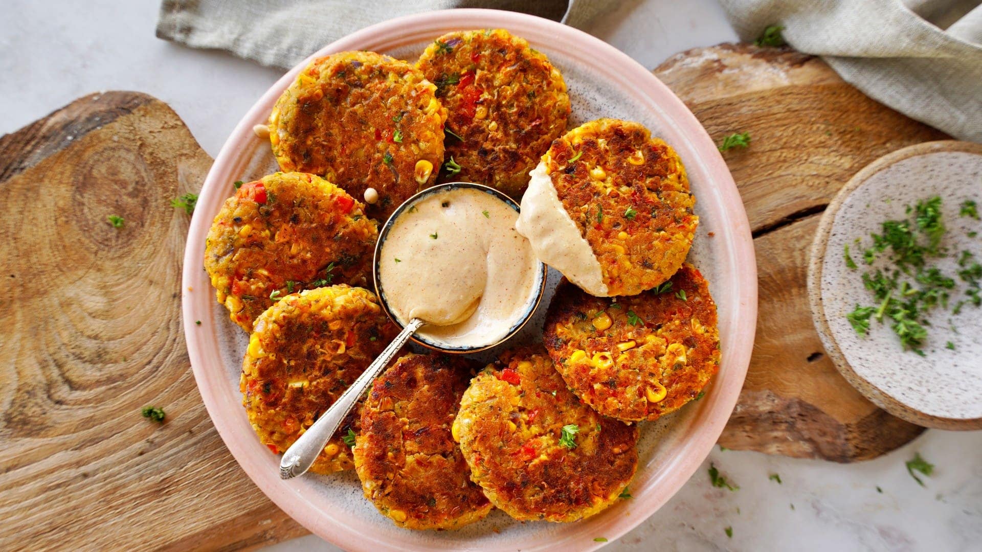 horizontal of 8 veggie chickpea fritters on plate with white dip in the middle