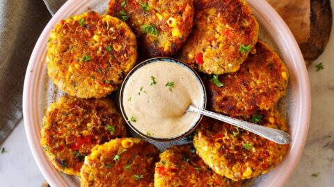 top shot of 8 veggie chickpea fritters on plate with creamy white dip in the middle