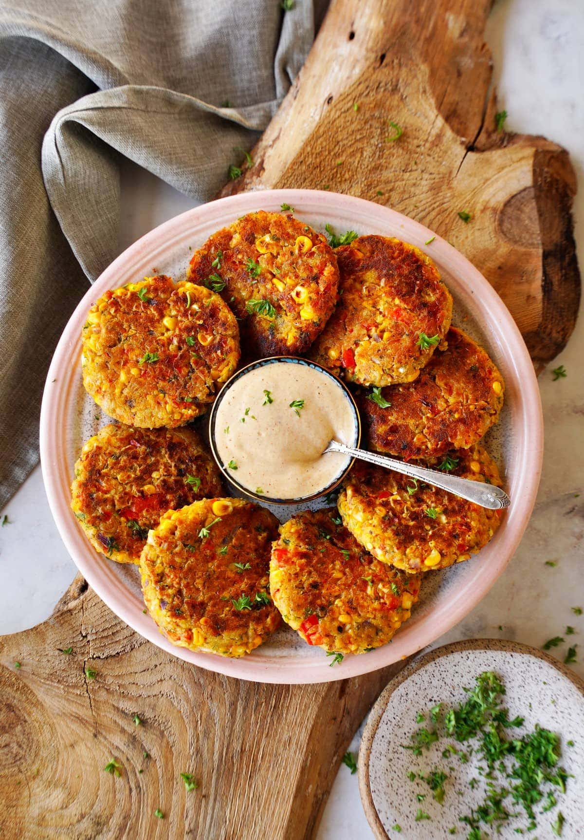 top shot of 8 veggie chickpea fritters on plate with creamy white dip in the middle