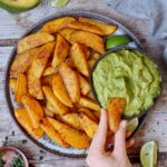 hand grabbing potato wedges on plate with guacamole