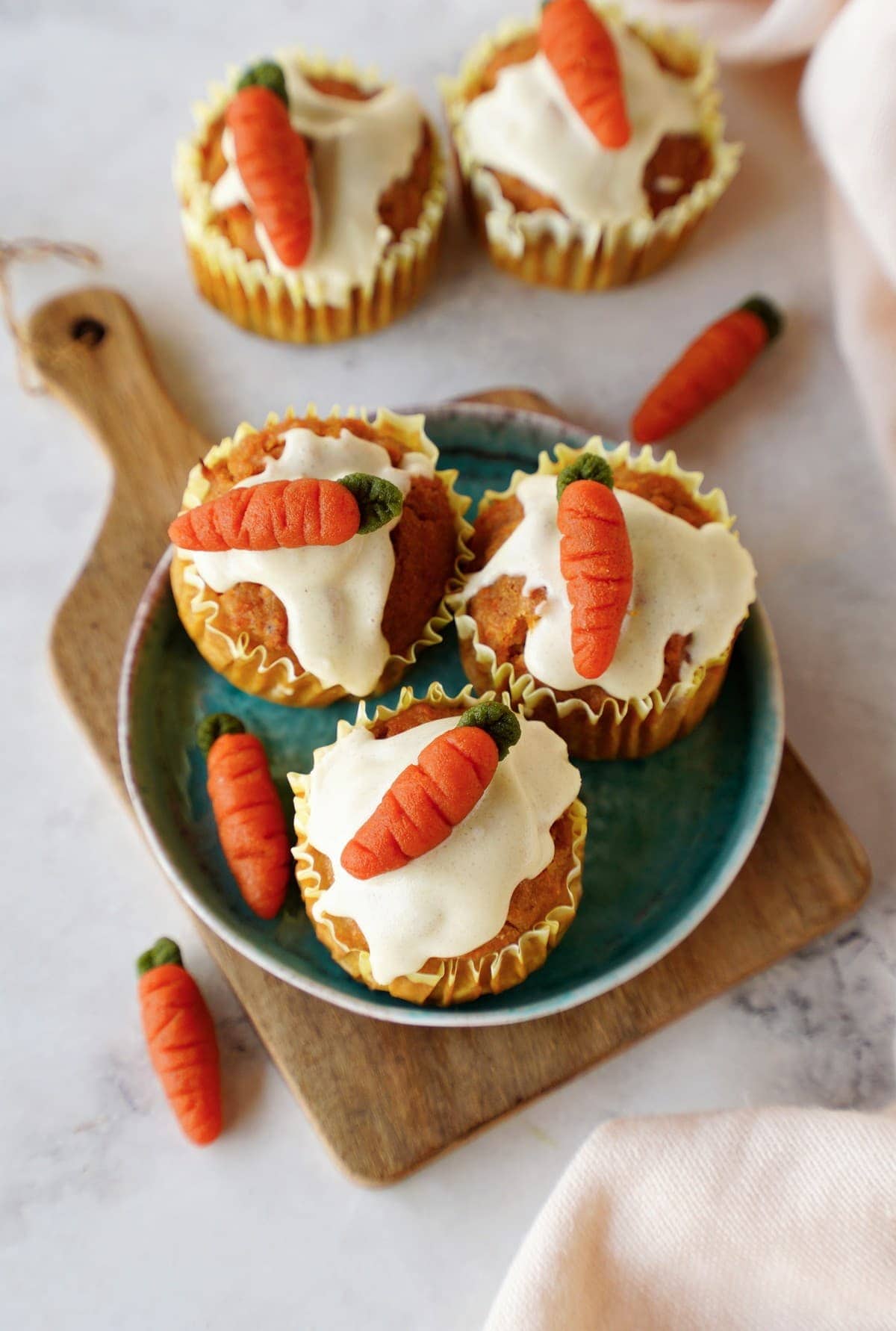 top shot of egg-free carrot muffins with icing and marzipan carrots on small plate