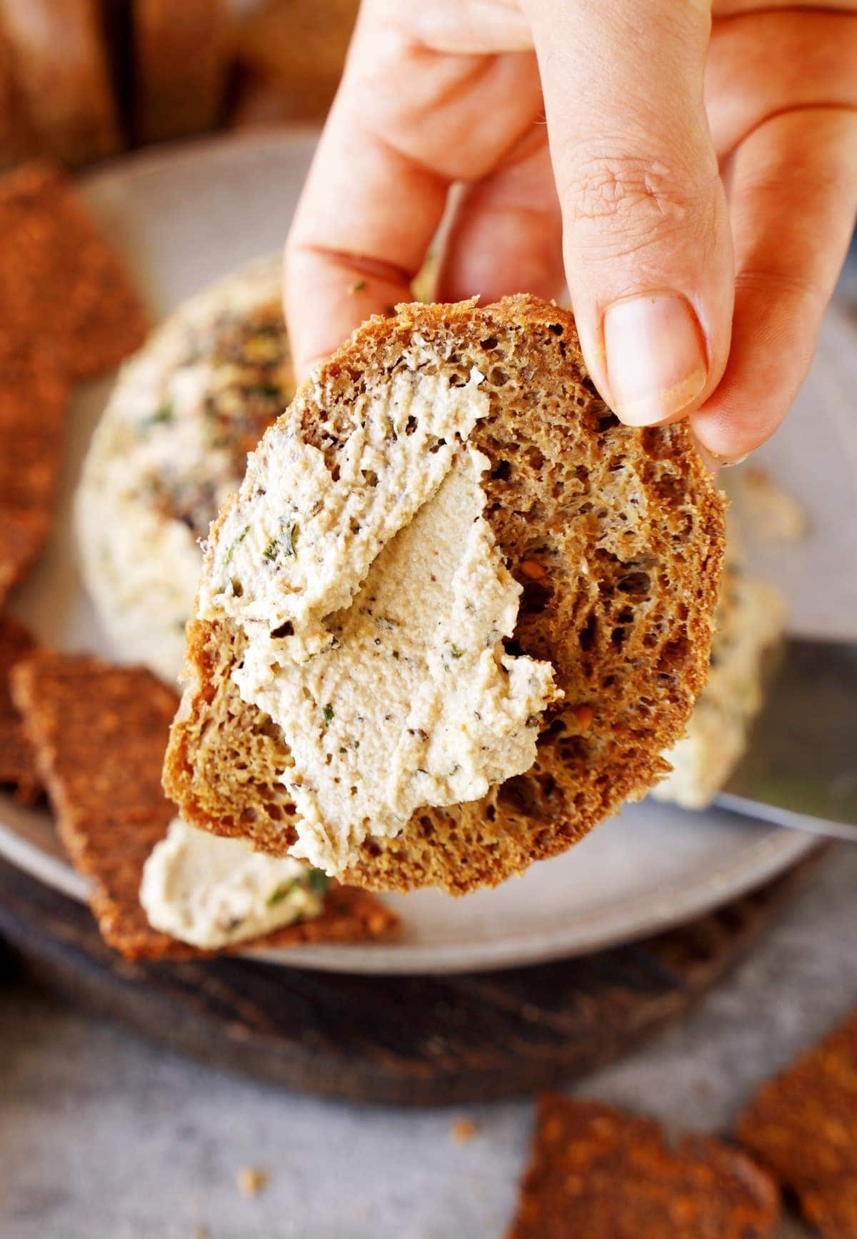 Hand hält ein Stück glutenfreies Brot mit veganem Frischkäse