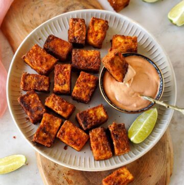 Air fried tofu on a white plate with creamy dip and lemon wedges