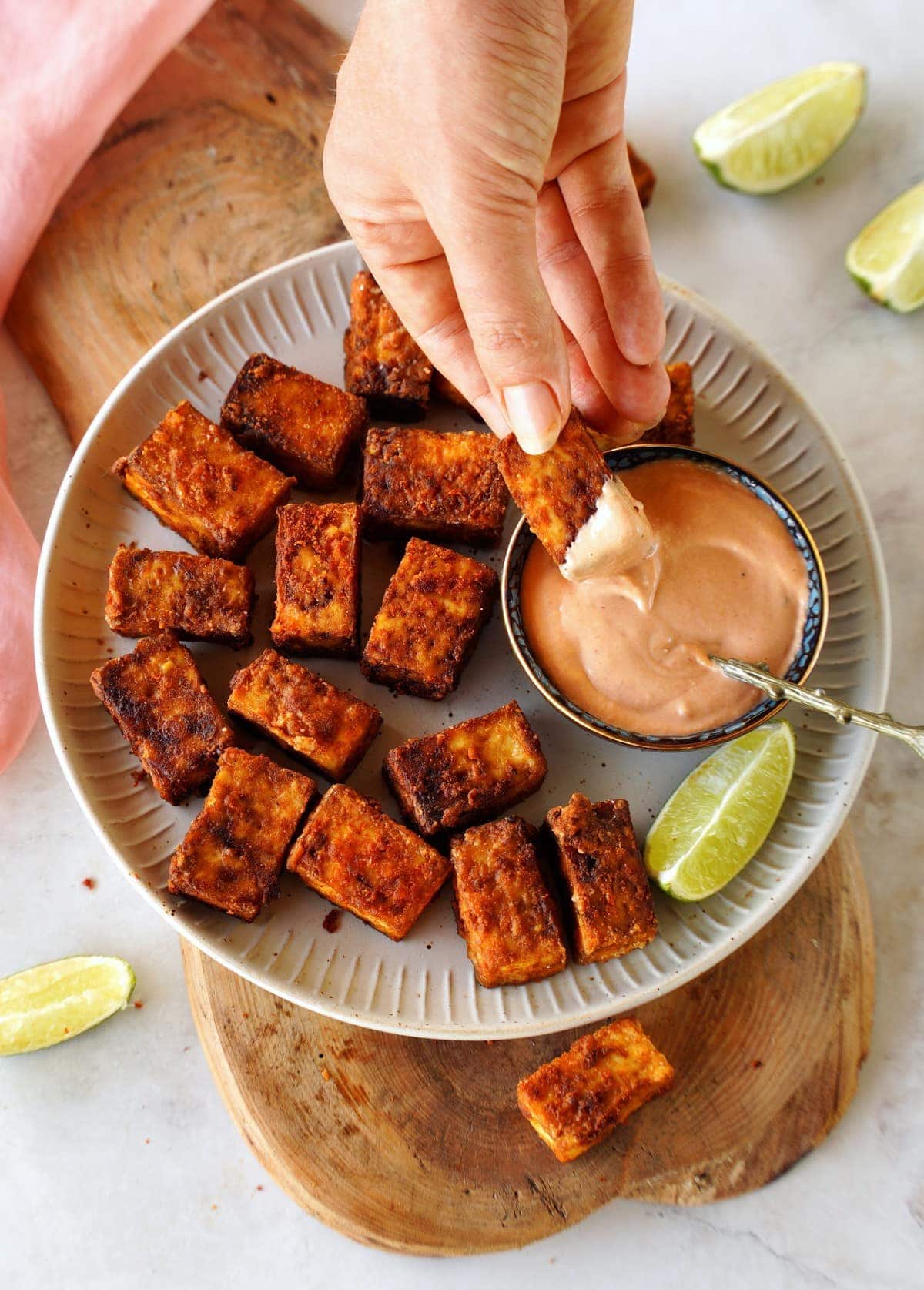 hand dipping a piece of air fried tofu into creamy sauce