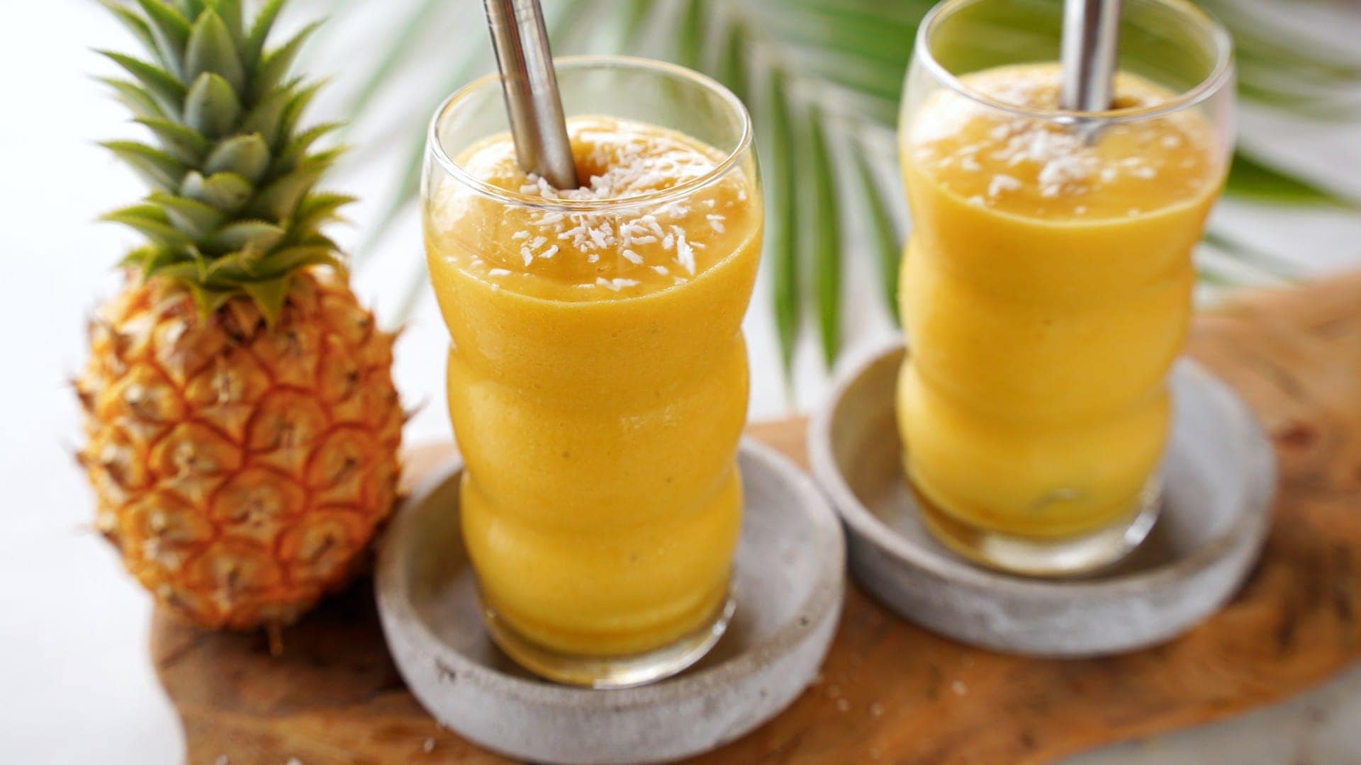 horizontal shot of mango pineapple smoothie in 2 glasses with straws