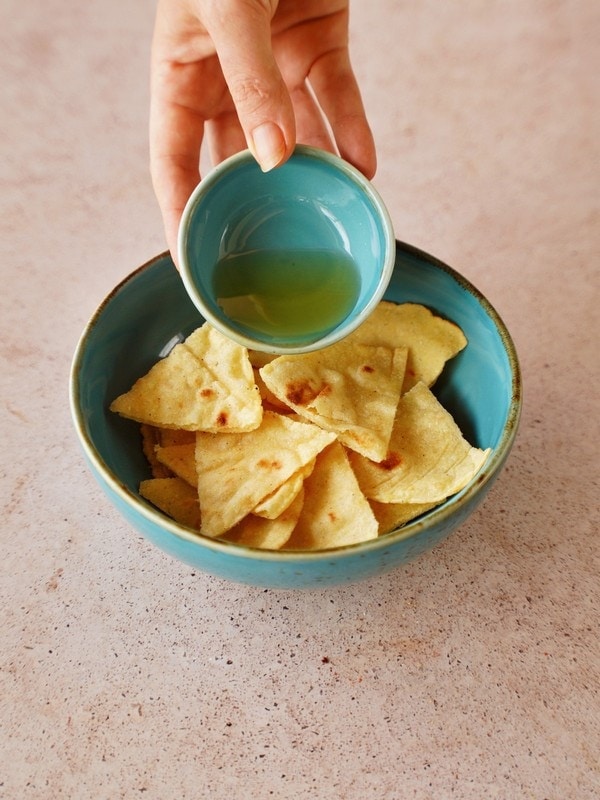 drizzling oil over corn tortilla triangles in blue bowl