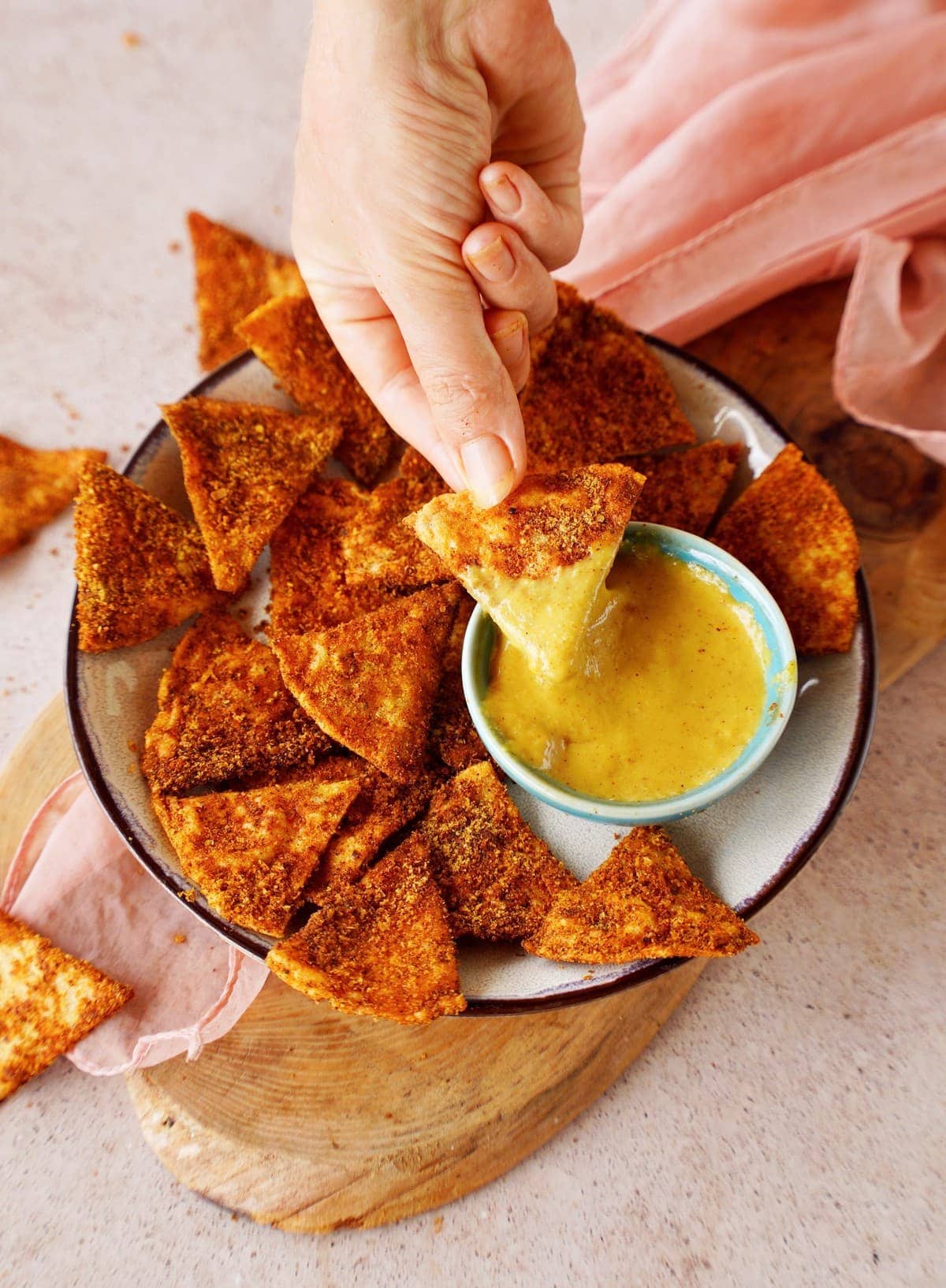 hand grabbing a homemade dorito tortilla chip dipped in nacho cheese