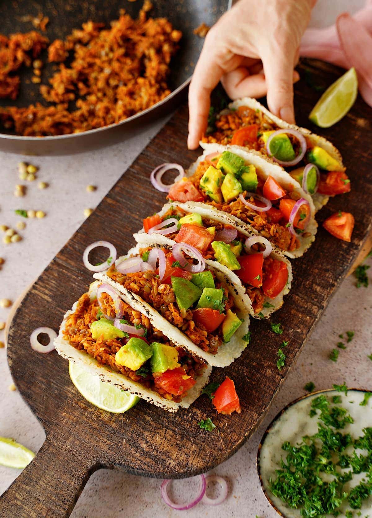 Hand greift nach einem Linsen-Hackfleisch-Taco mit Gemüse-Topping