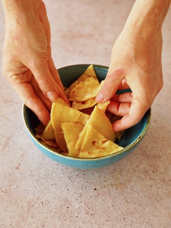 hands mixing corn tortilla triangles with oil in blue bowl
