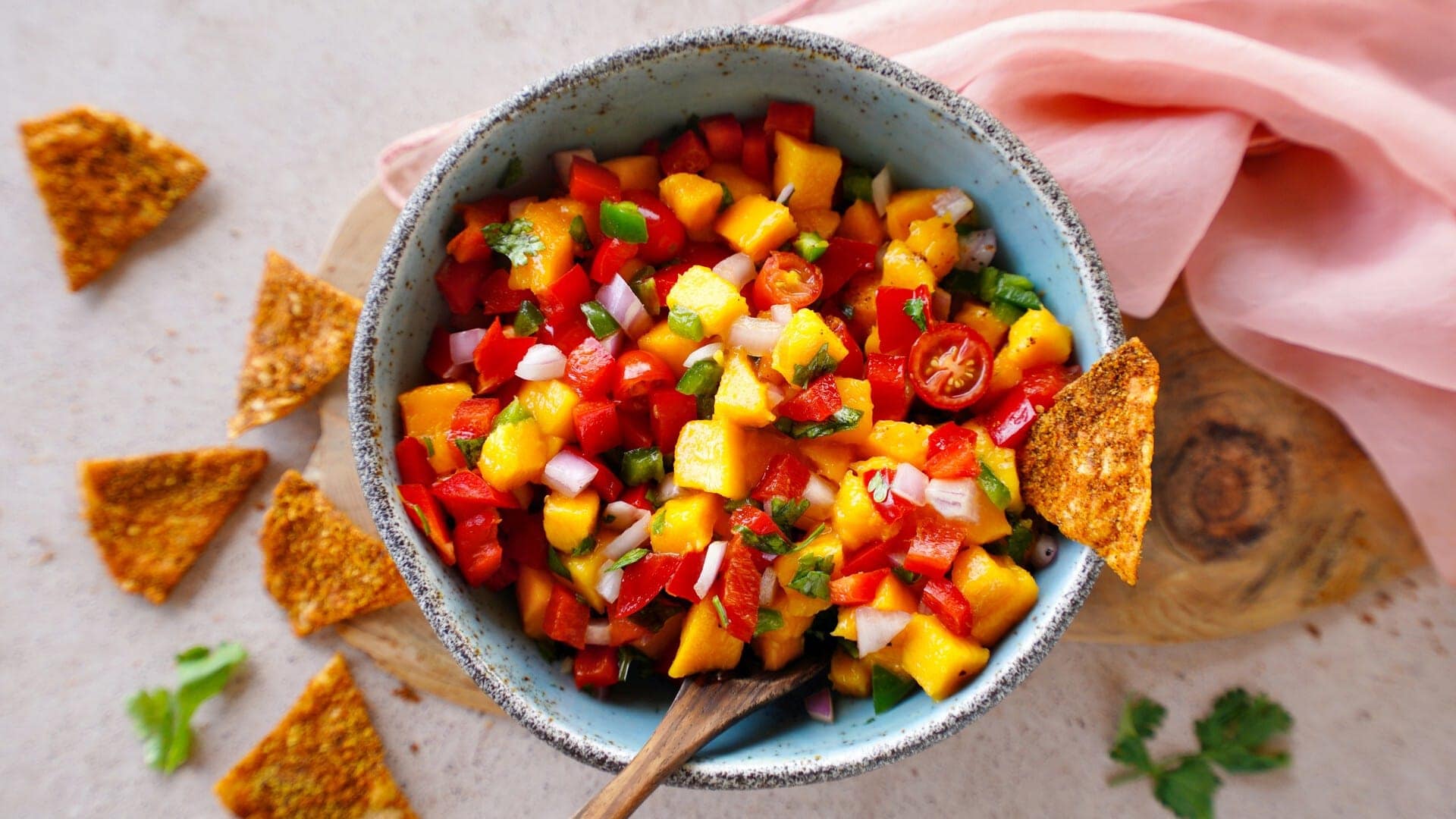 horizontal shot of mango salsa in bowl with wooden spoon and homemade doritos