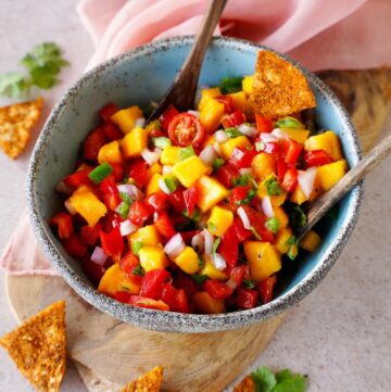 mango salsa in bowl with wooden spoons and tortilla chips