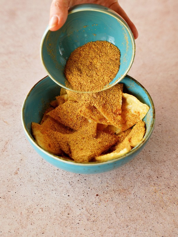 sprinkling spice mixture over corn tortilla triangles in blue bowl