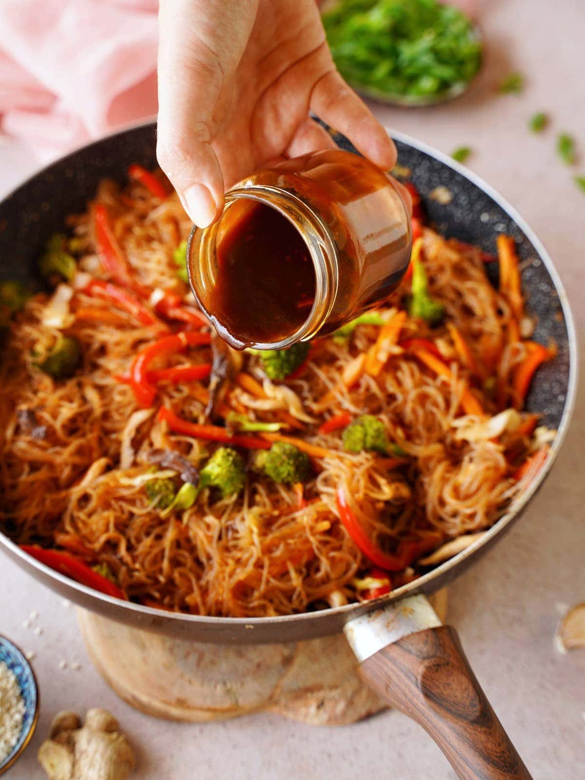 drizzling Korean BBQ sauce over veggie noodle stir-fry