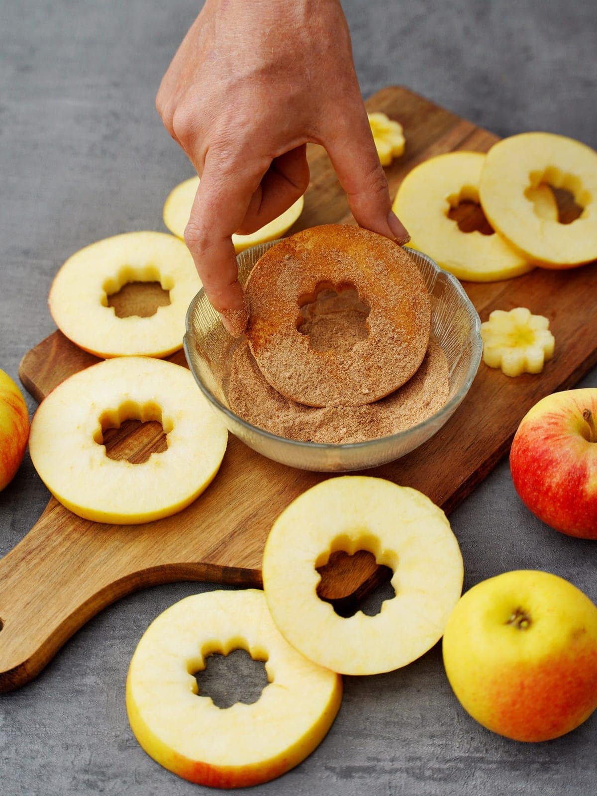 dipping cored apple slices into bowl with cinnamon sugar