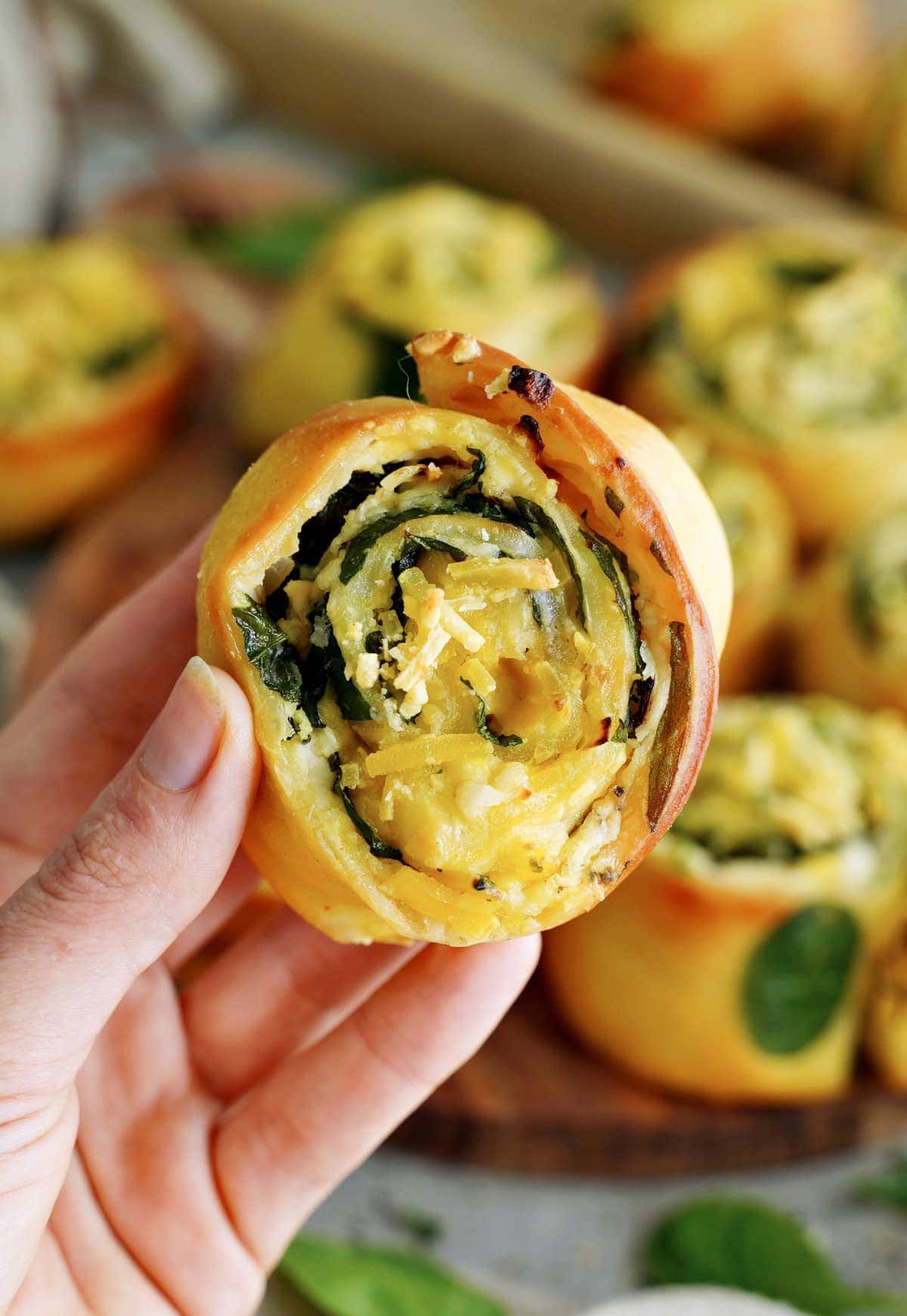 hand holding a spinach cheese pizza pinwheel