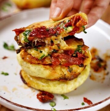 hand holding stuffed flatbread with sun-dried tomatoes and cheese