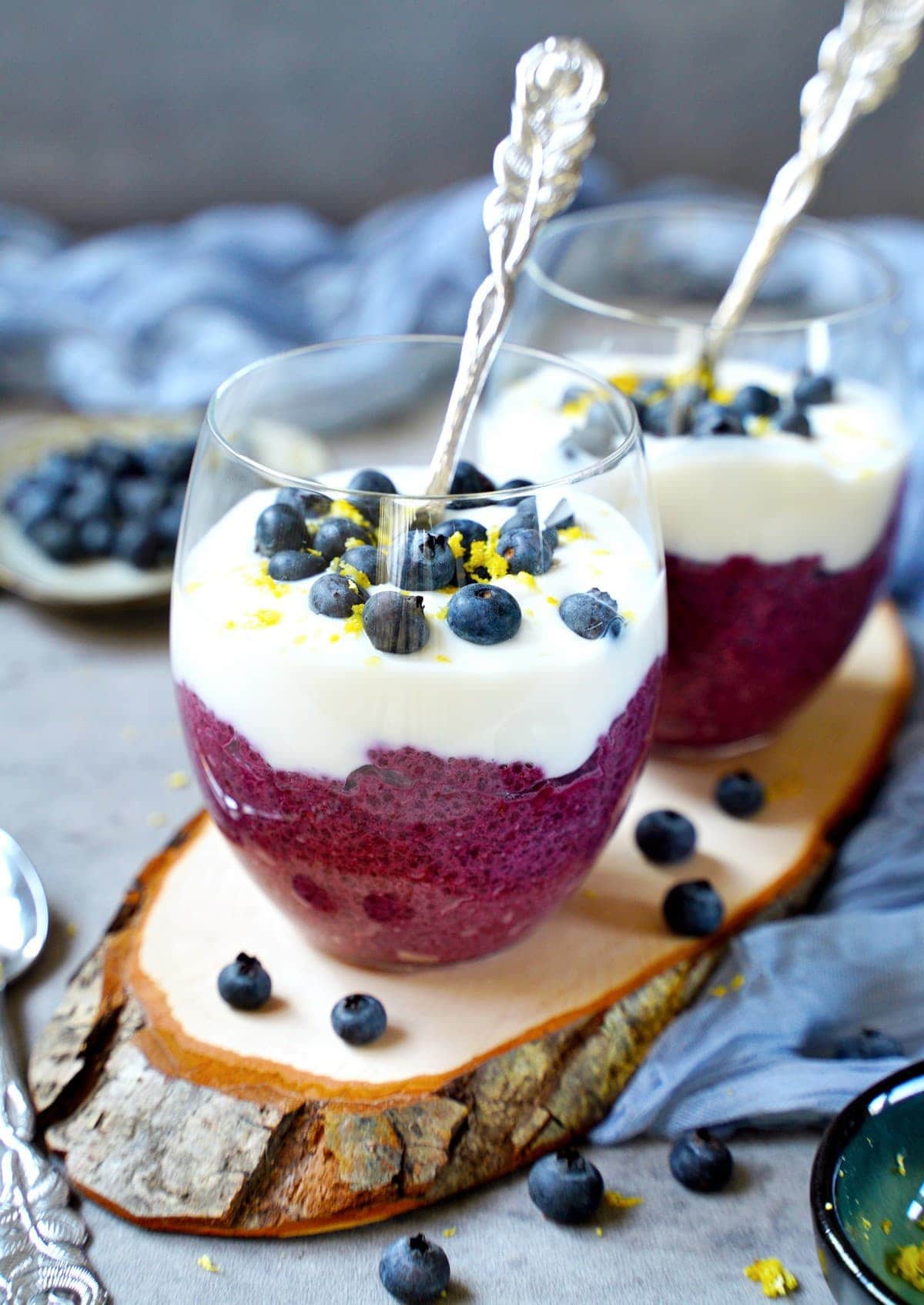 blueberry chia pudding with spoons in two jars with yogurt and fresh berries