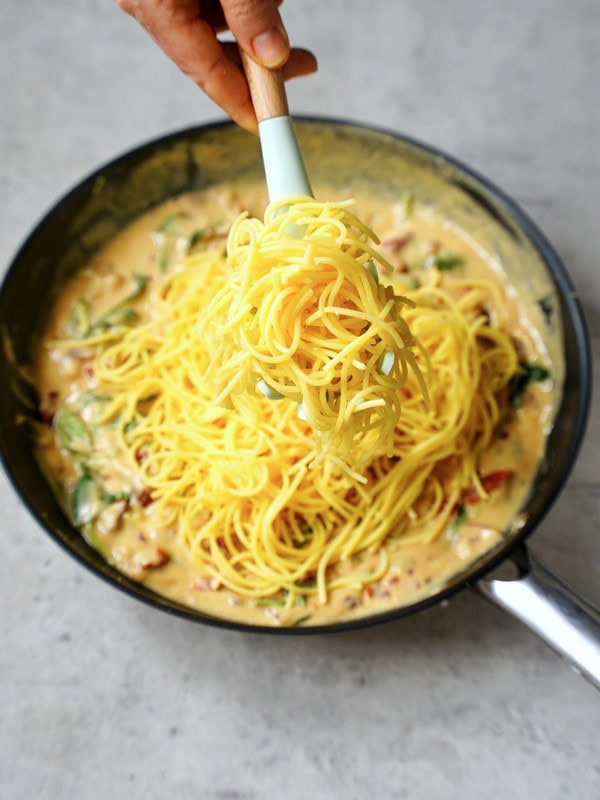 adding spaghetti to creamy sauce in skillet