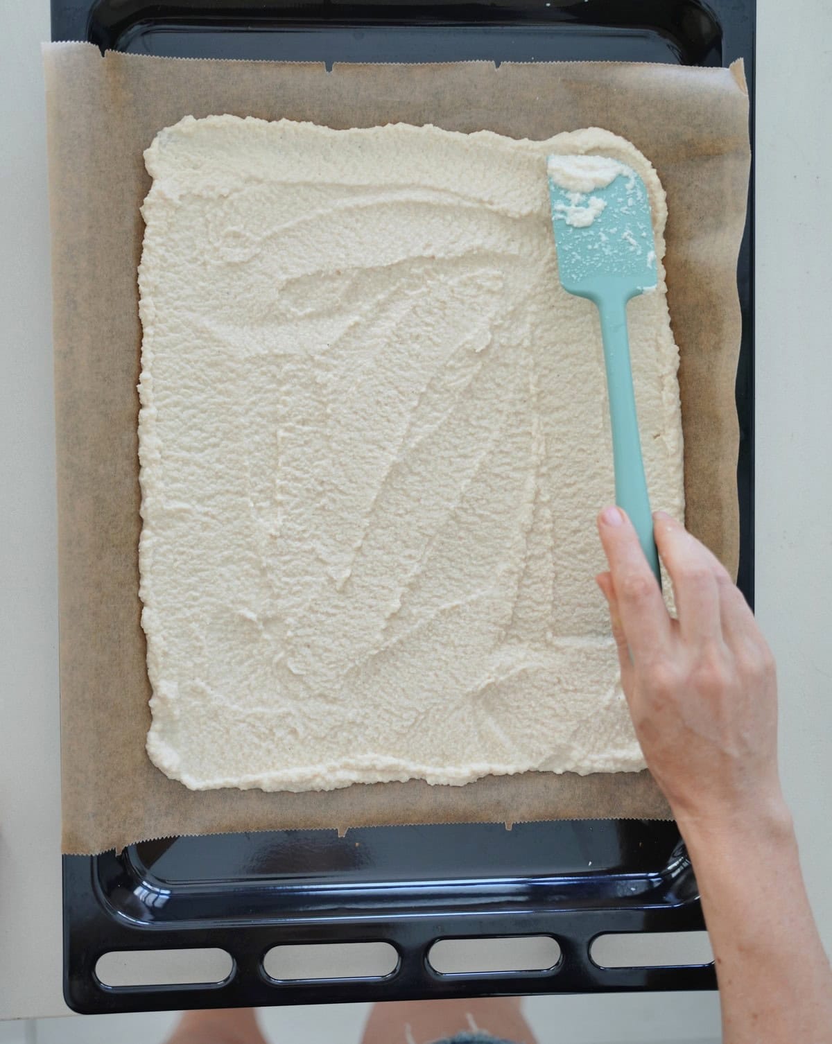 Hand spreads creamy mixture evenly on parchment paper with a spatula