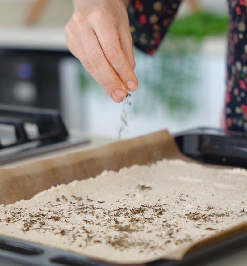 sprinkling italian herbs over chickpea chips batter