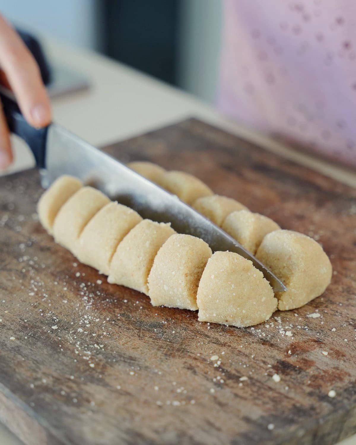 Eine Hand schneidet Mandelhörnchen-Teig auf einem Holzbrett in zwölf gleichmäßige Stücke