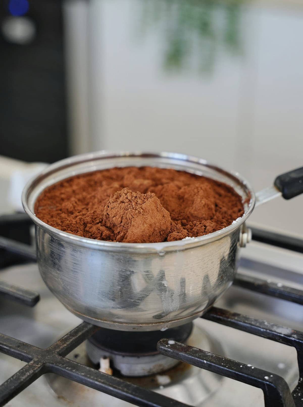 A pot filled with rich, brown cocoa powder sits on a stovetop burner