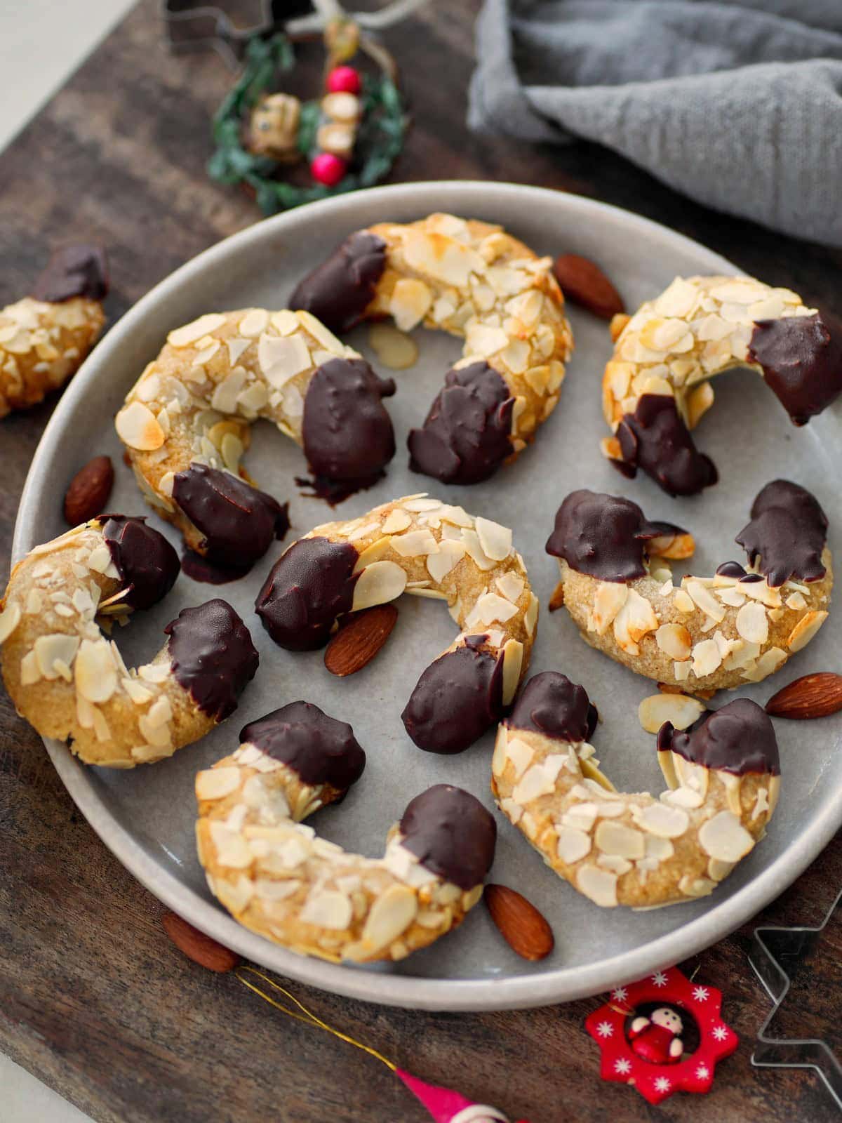 Ein runder Teller mit in Schokolade getauchten Mandelhörnchen steht auf einem Holzbrett