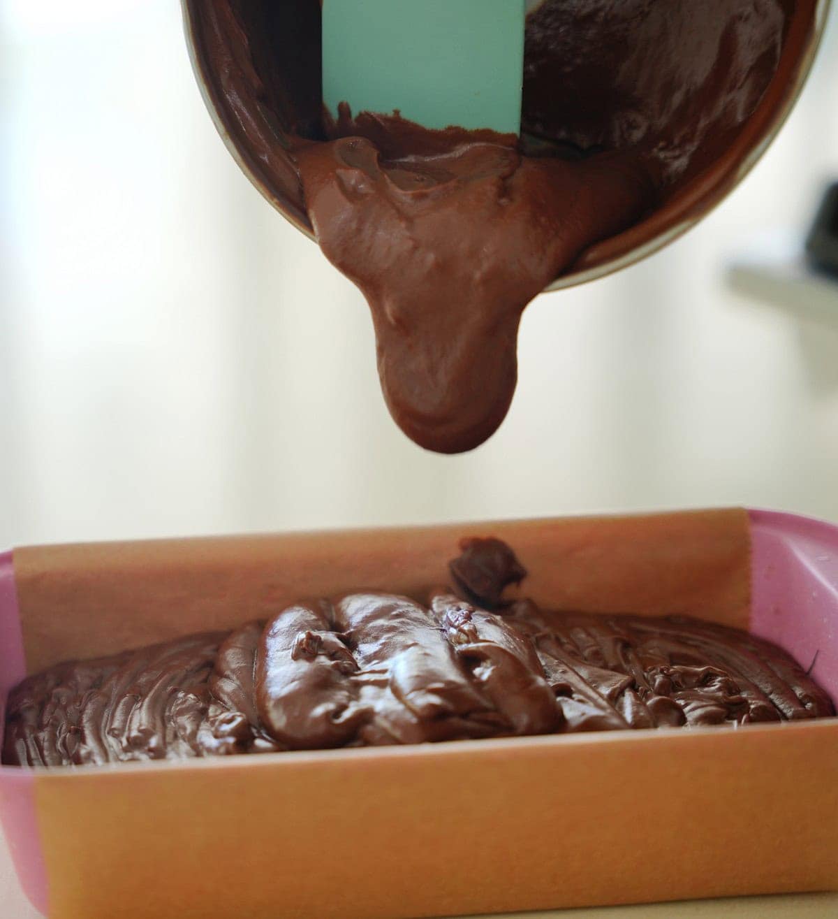 Chocolate batter is being poured from a pot into a parchment-lined baking tin