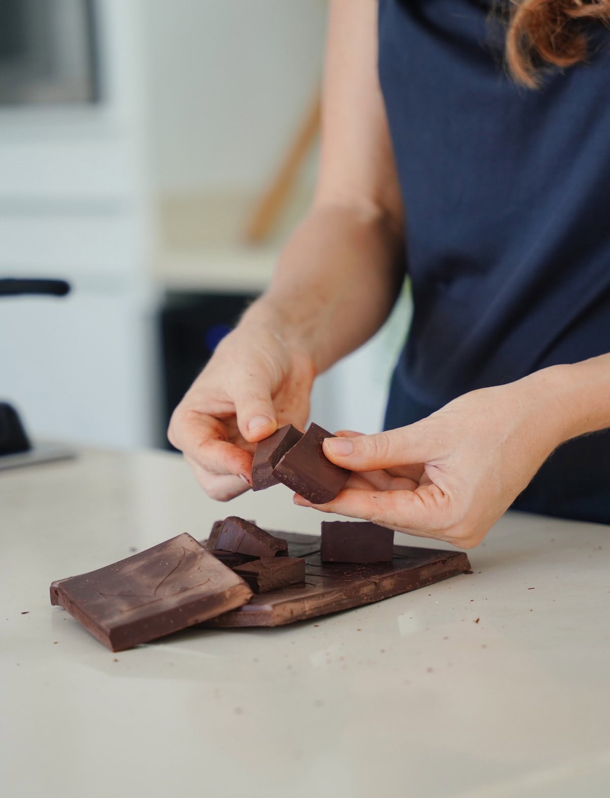 Elavegan breaks a bar of chocolate into chunks on a light kitchen counter
