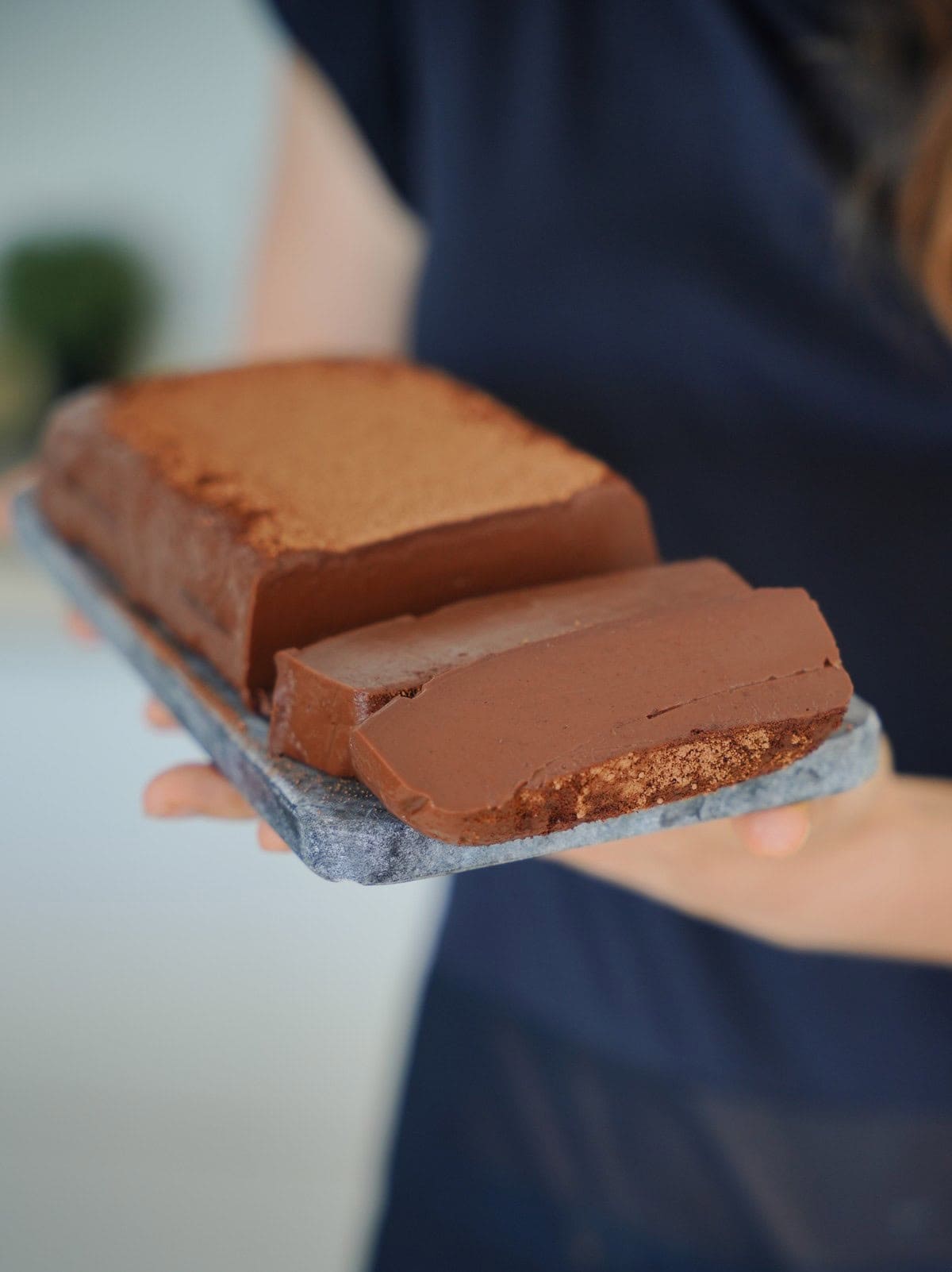 Elavegan holding a rectangular chocolate mousse cake on a stone tray. The cake has a smooth texture