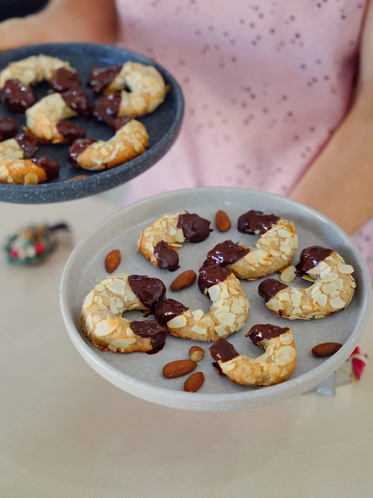 Elavegan hält zwei Teller mit in Schokolade getauchten Mandelhörnchen