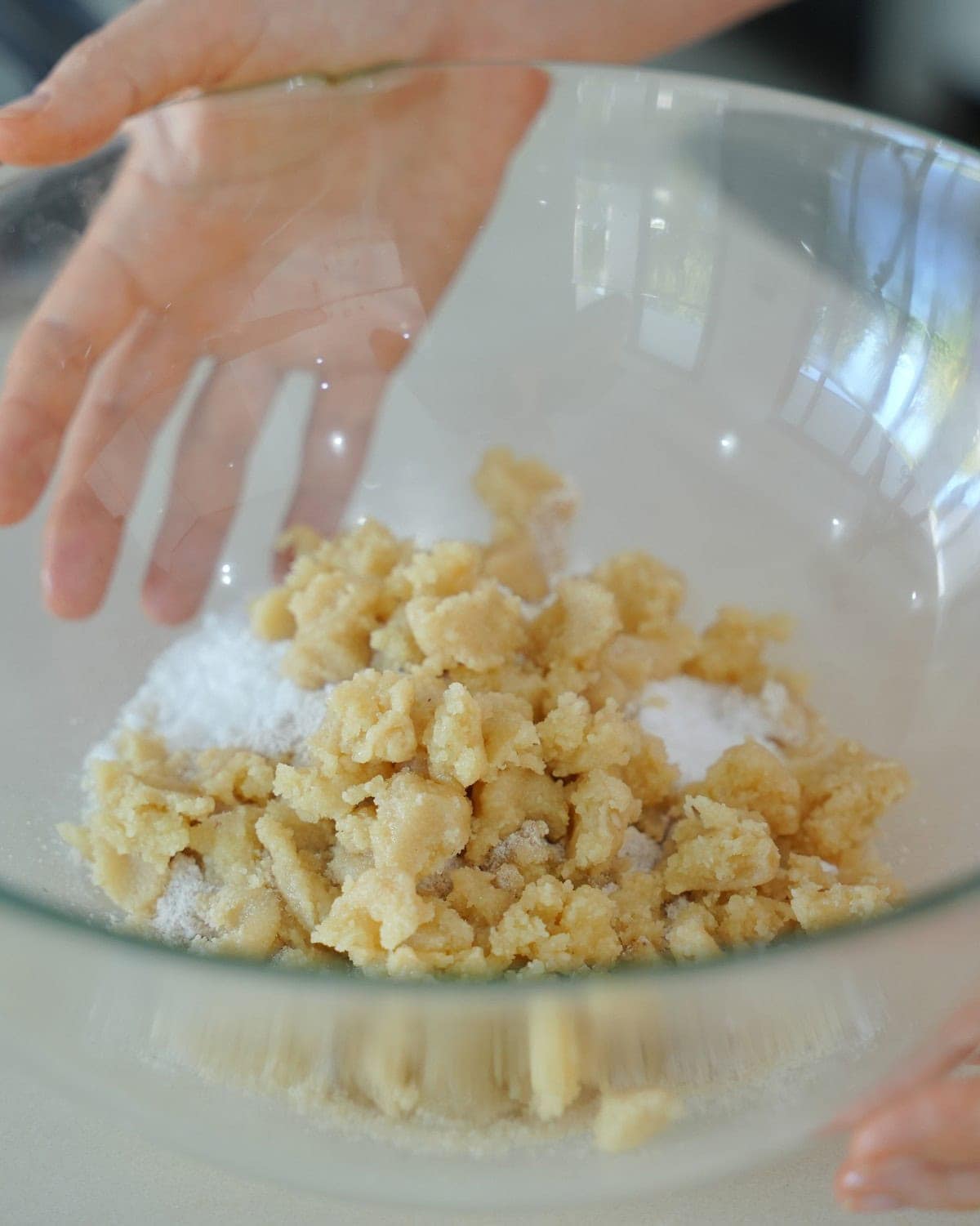 Hände vermengen Marzipan und Puderzucker in einer durchsichtigen Glasschüssel