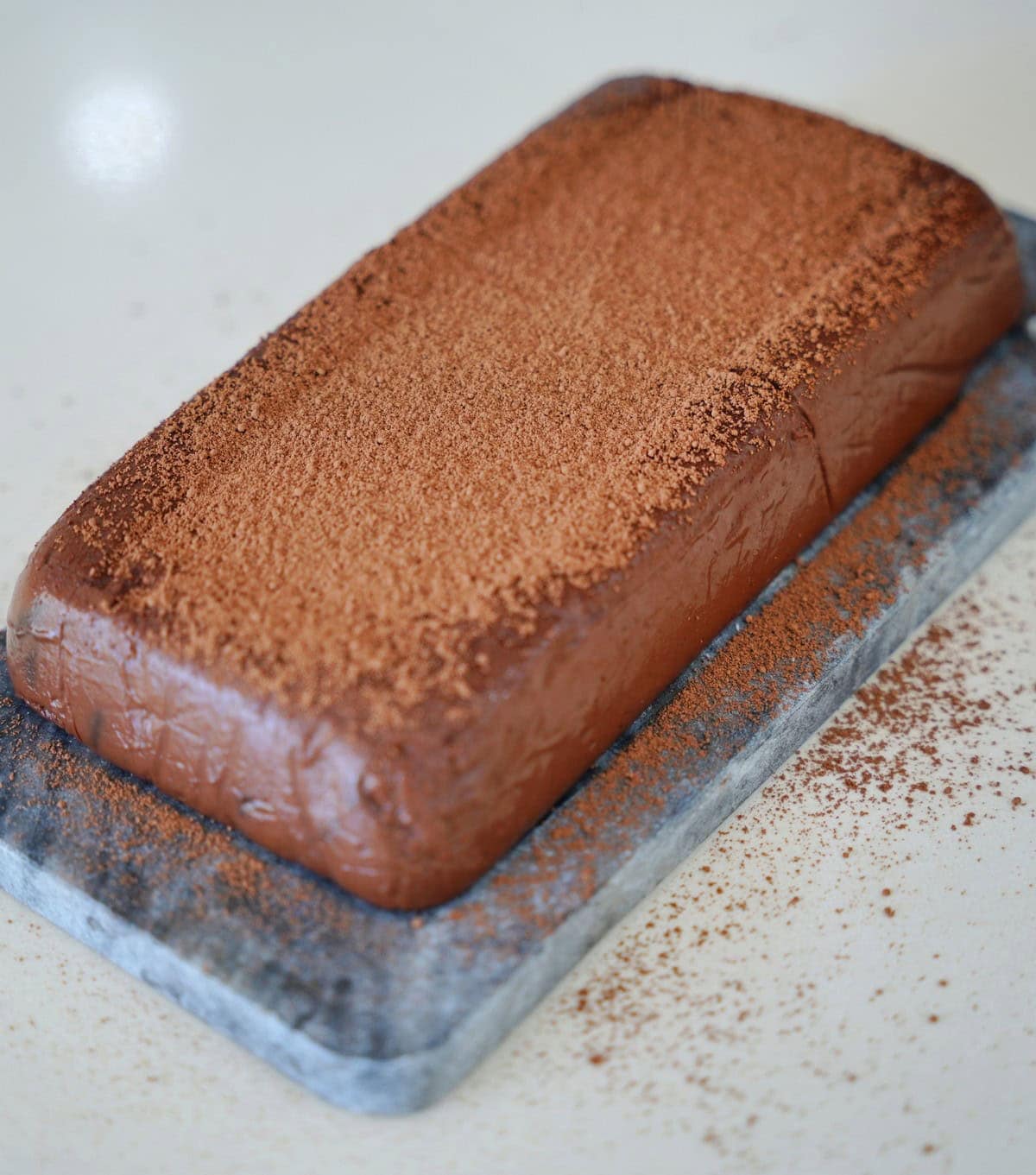 Rich chocolate pudding cake dusted with cocoa sits on a gray slate board