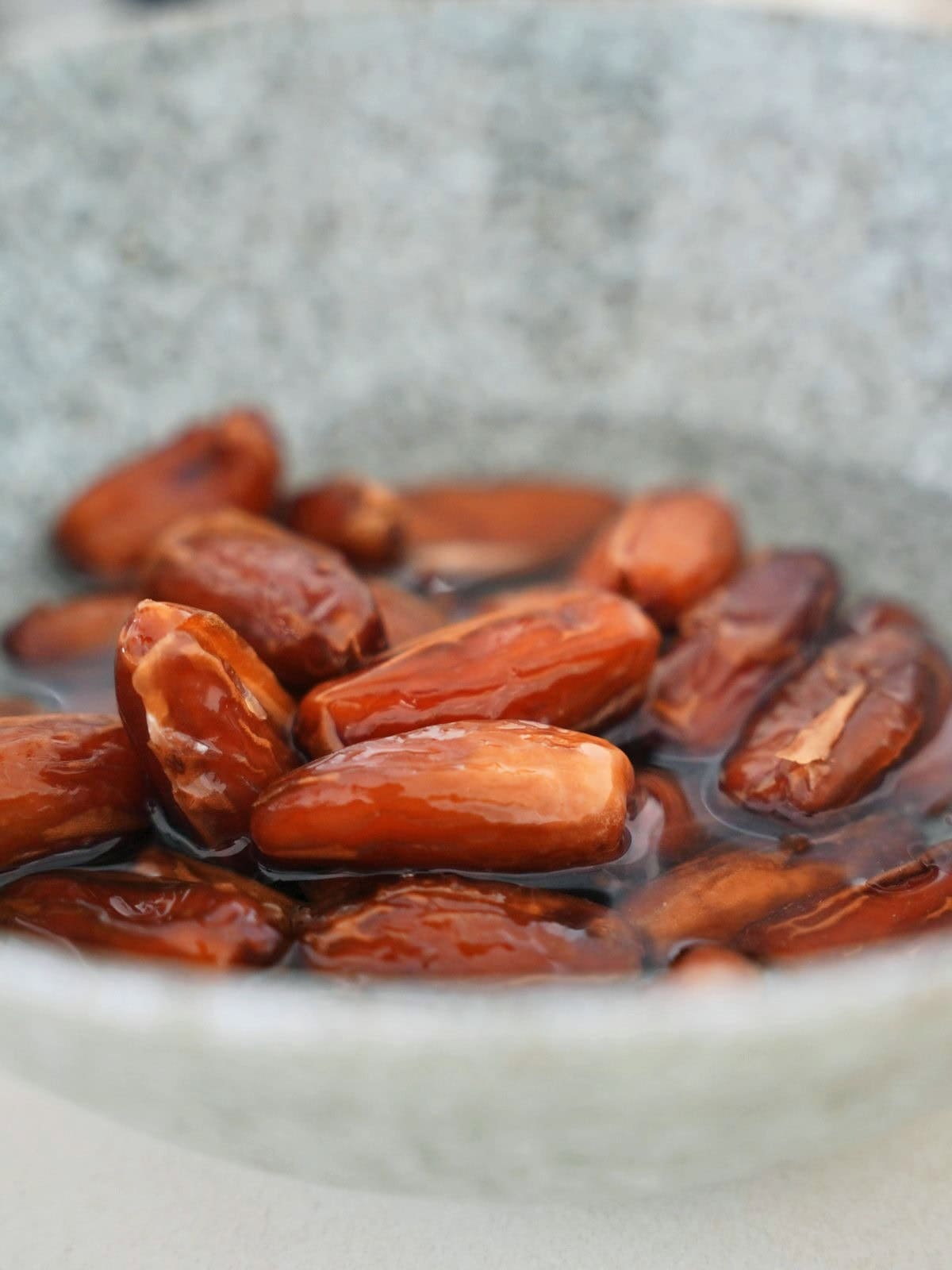A bowl filled with glossy brown dates soaking in water