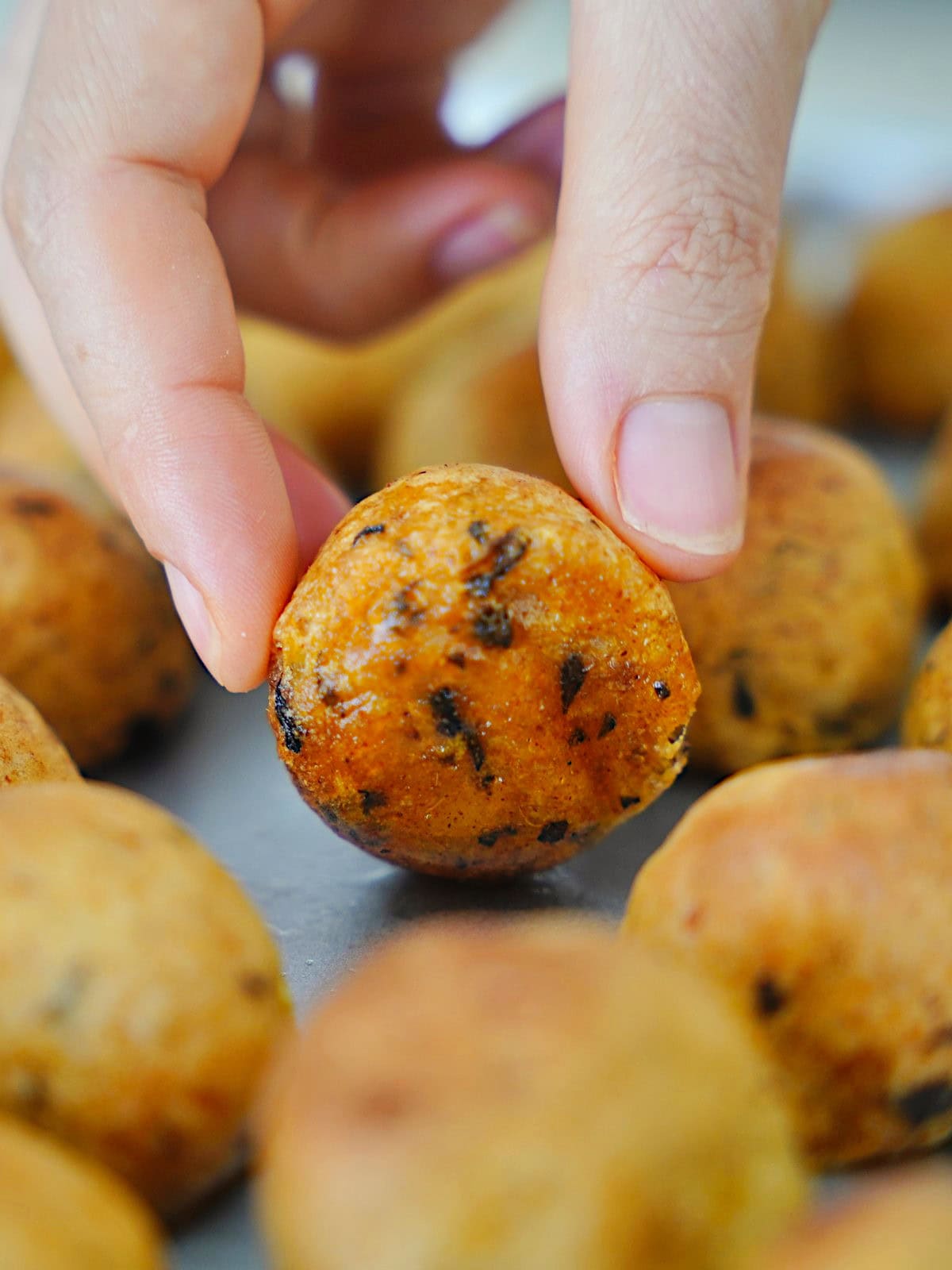 A hand holds a golden-brown, round crispy potato ball with visible herbs